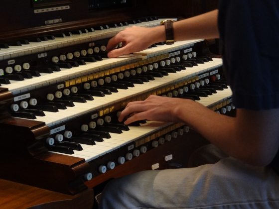 A person in a black shirt sitting at an organ playing the keys.
